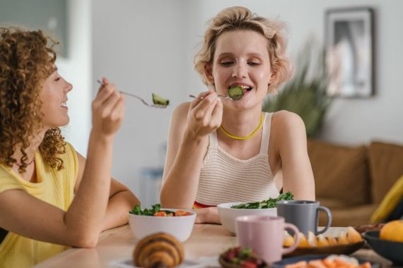 Two women enjoying a healthy meal at a cozy dining table, sharing a joyful indoor breakfast moment.